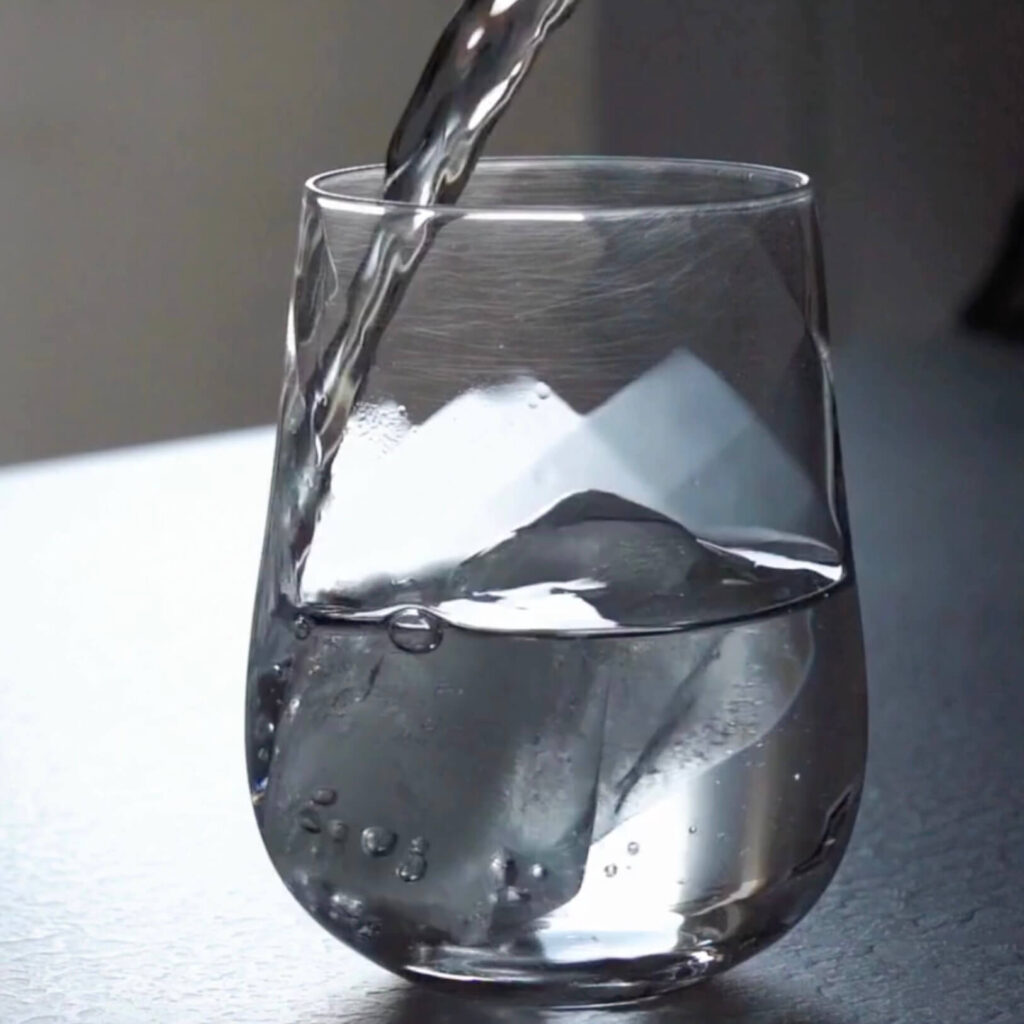 a clear stemless glass sitting on a table that is half full with water being poured into it